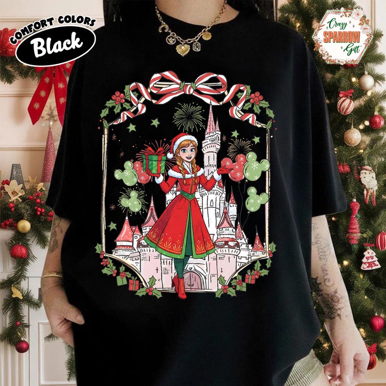 Może przedstawiać: Czarny t-shirt z motywem świątecznym. Grafika przedstawia postać z kresk&oacute;wki w czerwonym płaszczu i czapce Świętego Mikołaja trzymającą prezenty i balony przed zamkiem. Koszulka ma napis "Comfort Colors Black".
