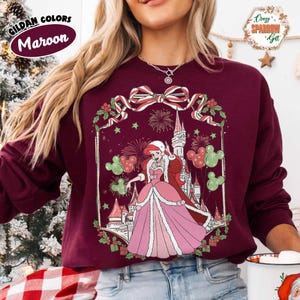 May include: Maroon sweatshirt with a princess illustration in a pink gown and a castle, Mickey Mouse balloons and fireworks. The sweatshirt has the text "Gildan Colors Maroon" on the upper left.