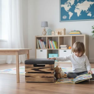 May include: A child's room with a wooden table and stool, a storage ottoman, and a bookshelf. The child is sitting on the floor reading a book. A stuffed bear is next to the child. The room has a world map on the wall.