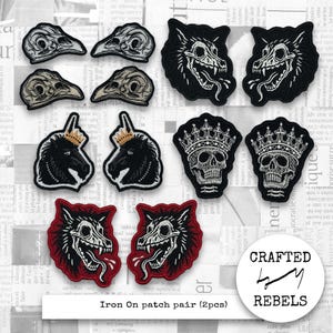 Pode incluir: Uma coleção de patches termocolantes com vários designs. Incluem-se patches de crânios de pássaros, patches de lobos, patches de crânios com coroas e patches de cavalos com coroas. Os patches são pretos, brancos e vermelhos. O texto "Iron On patch pair (2pcs)" é visível.
