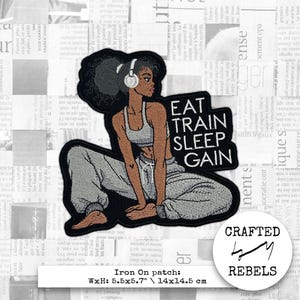 May include: An iron-on patch featuring a stylized illustration of a woman in workout attire wearing headphones. The patch includes the text "EAT TRAIN SLEEP GAIN". The patch measures 5.5 x 5.7 inches.
