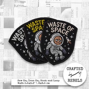 May include: Black embroidered patch featuring the words "WASTE OF SPACE" and an astronaut illustration. The patch measures 6.35cm x 8.38cm. The astronaut has a sad expression. The patch can be sewn, ironed, or attached with hook and loop.