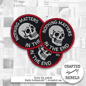 Puede incluir: Parches negros termoadhesivos con un diseño de calavera blanca y el texto "NOTHING MATTERS IN THE END" en formato circular. Cada parche mide 6,5 x 6,5 cm. Los parches son de Crafted Rebels.