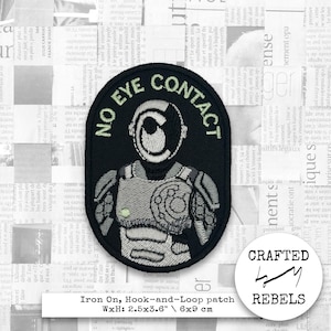 Può includere: Toppa rettangolare nera con la scritta "NO EYE CONTACT" e un'illustrazione a forma di robot. La toppa misura 6 x 9 cm ed è una toppa termoadesiva, a strappo.