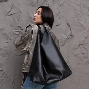 Puede incluir: Un bolso hobo negro grande con textura granulada y silueta holgada. El bolso cuenta con una correa ancha para el hombro y un compartimento principal espacioso, confeccionado con un material flexible que se ajusta al hombro.