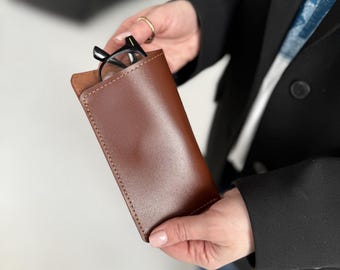 Puede incluir: Un estuche de gafas de cuero marrón con un par de gafas dentro.