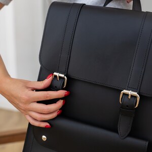 May include: Black leather backpack with silver buckles and a front pocket. The bag has a top handle and adjustable straps. The design is simple and classic, suitable for everyday use.