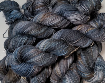 May include: A pile of hand-dyed yarn in shades of blue, gray, and brown. The yarn is twisted into skeins, showing variations in color and texture. The yarn appears soft and is suitable for knitting or crochet projects.