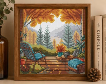 May include: A framed cross-stitch embroidery depicting a scenic autumn balcony view. The scene features a blue chair, a small table with a teapot, and potted plants overlooking a landscape of evergreen trees and golden foliage under a mountain range.