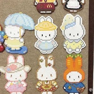 May include: A collection of twelve pixel art figures made from plastic beads, each depicting a white rabbit character in various outfits including a fast-food uniform, a maid costume, a yellow raincoat, a waffle suit, and seasonal attire.