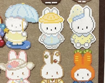 Può includere: Una collezione di dodici figure in pixel art realizzate con perline di plastica, ognuna raffigurante un coniglio bianco in vari abiti, tra cui un'uniforme da fast food, un costume da cameriera, un impermeabile giallo e un costume da waffle.