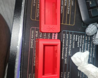 Pode incluir: Dois chaveiros de plástico vermelho com um anel de metal preto. Os chaveiros são retangulares e têm um pequeno recorte retangular no centro. O texto "BJORN" está impresso na parte inferior do chaveiro.