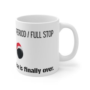 Puede incluir: Taza de cerámica blanca con el texto "PERIOD / FULL STOP" y "The noise is finally over". Un pequeño gorro de Papá Noel y unos auriculares negros están impresos en la taza. La taza tiene un asa blanca.