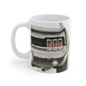 May include: White ceramic mug featuring a black and gray illustration of the rear of a classic muscle car. The car's taillights are red, and the exhaust pipe is visible. A unique gift for car enthusiasts.