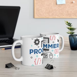 Puede incluir: Dos tazas de café blancas con la palabra "PROGRAMMER" en azul y negro, junto con iconos relacionados con la informática. Las tazas están sobre una superficie clara, con un portátil y material de oficina en el fondo.