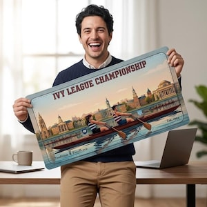 Puede incluir: Un letrero rectangular con el texto "IVY LEAGUE CHAMPIONSHIP" y una ilustración vintage de un equipo de remo en un río. El letrero tiene un borde azul claro y un fondo de paisaje urbano. El letrero lo sostiene una persona.