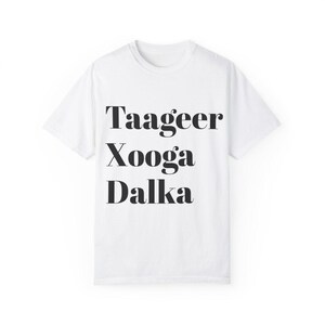 Peut inclure: T-shirt blanc avec du texte noir qui dit "Taageer Xooga Dalka"