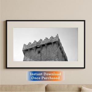 May include: Black and white photograph of a stone castle tower against a cloudy sky.