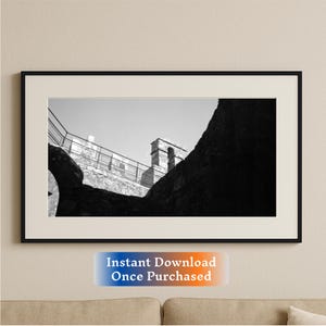 May include: Black and white photograph of a stone building with a tower. The photo is taken from a low angle, looking up at the tower. The building is partially obscured by a large rock.
