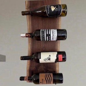 May include: A wooden wine rack displaying four wine bottles. The rack is made of a dark wood slab with a natural edge. Each bottle is held in place by a black metal holder. The bottles have various labels.