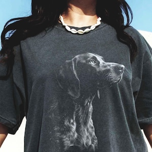 May include: An oversized t-shirt in a dark grey colour with a white graphic of a German Shorthaired Pointer dog's head. The text "PEPPER" is visible in the bottom left corner of the image.