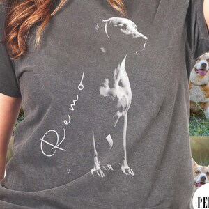 May include: A charcoal grey t-shirt with a white silhouette of a dog and the name "Remo" written in cursive.