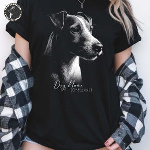 May include: Black t-shirt featuring a detailed black and white illustration of a dog's head. The text "Dog Name (optional)" is written in a cursive font. The shirt has short sleeves.