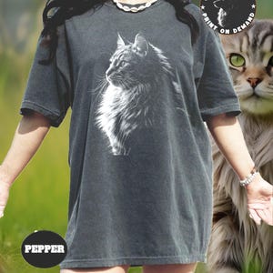 May include: A dark gray oversized t-shirt with a white graphic of a cat's head. The text "PRINTSYHAVEN PRINT ON DEMAND" is on a black circle on the upper right corner of the shirt. The text "PEPPER" is on a black circle on the bottom left corner of the shirt.