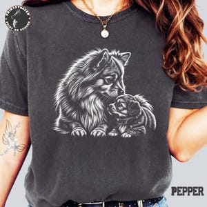 Peut inclure: T-shirt gris foncé avec une illustration blanche détaillée d'une chienne et de son chiot. Le motif montre les chiens proches l'un de l'autre, la mère chien reniflant le chiot. Le mot "PEPPER" est imprimé en bas à droite.