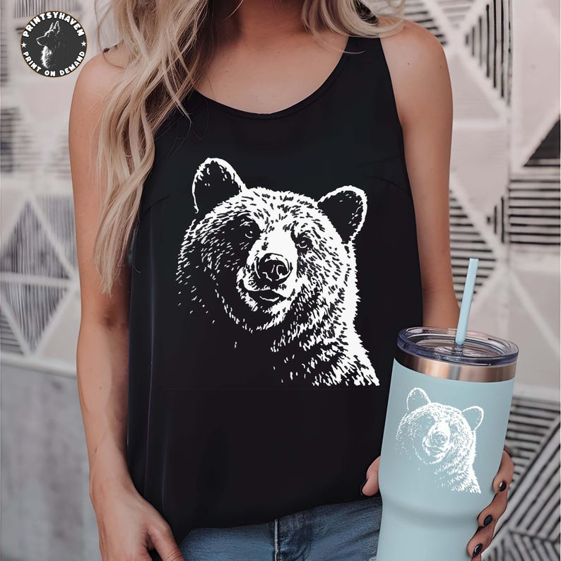Puede incluir: Camiseta sin mangas negra con un gr&aacute;fico de oso blanco. Tambi&eacute;n se ve un vaso azul claro con un dise&ntilde;o de oso a juego. La camiseta sin mangas y el vaso presentan una ilustraci&oacute;n de oso similar.