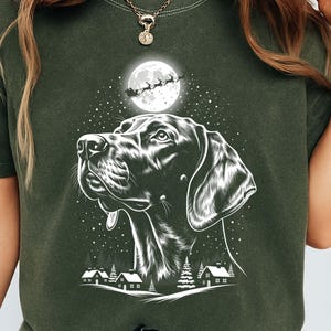 May include: Dark green t-shirt with a black and white illustration of a dog gazing upwards at a full moon and Santa's sleigh. The design includes a winter landscape with houses and trees. The word "HEMP" is printed at the bottom.