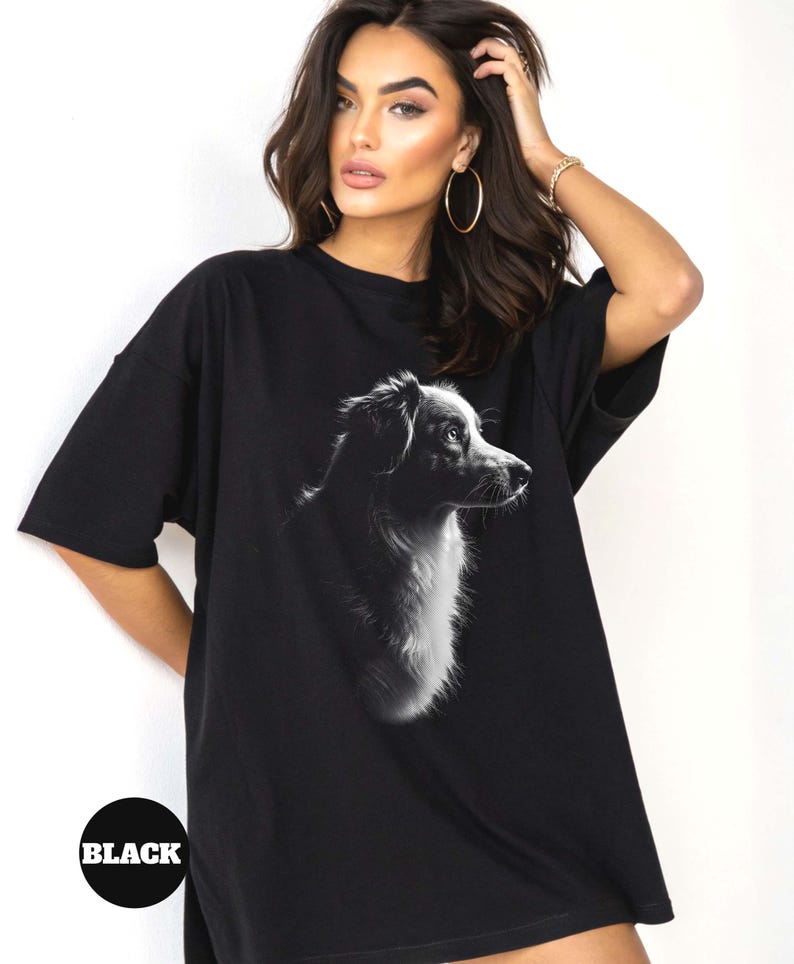 May include: Black oversized t-shirt featuring a black and white silhouette of a dog's head. The dog is looking to the right. The t-shirt has a crew neck and short sleeves.