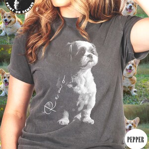 May include: A gray t-shirt with a white image of a Shih Tzu dog. The dog's name, "Remo", is written in cursive on the shirt. The shirt has a distressed look.