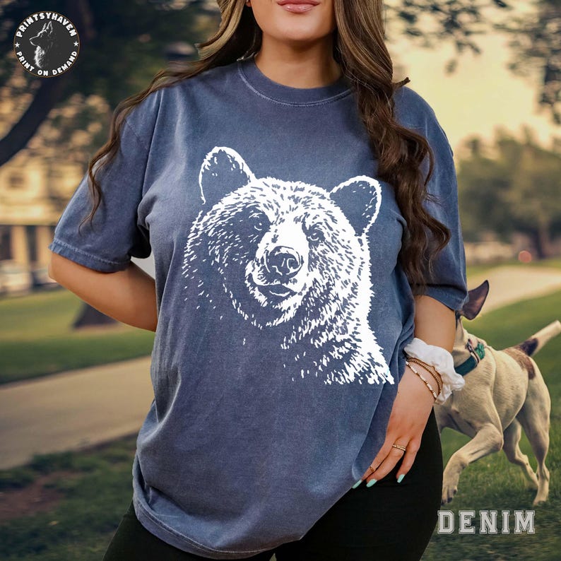 Puede incluir: Camiseta azul denim con un gr&aacute;fico de oso blanco. La camiseta tiene mangas cortas y cuello redondo. La palabra "DENIM" est&aacute; impresa en blanco en la esquina inferior derecha. El logotipo de PrintsyHaven es visible en la parte superior izquierda.
