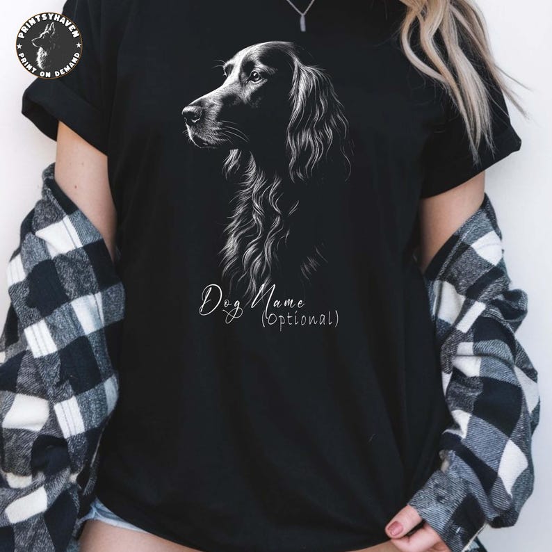 May include: Black t-shirt featuring a detailed white illustration of a dog's head and neck. The text "Dog Name (Optional)" is written in a cursive font below the illustration. The shirt has short sleeves.