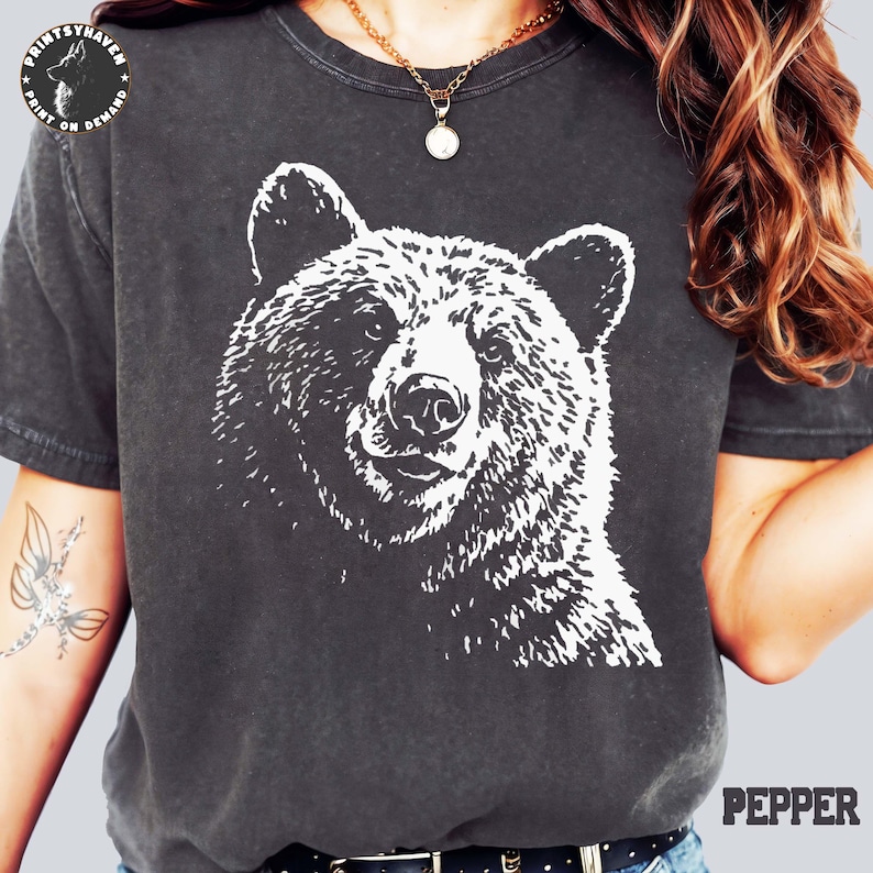Puede incluir: Camiseta gris oscuro con un gr&aacute;fico blanco detallado de la cara de un oso. La camiseta tiene un aspecto vintage y desgastado. La palabra "PEPPER" est&aacute; impresa en blanco en la parte inferior derecha. Una prenda casual.
