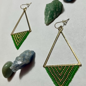 May include: Geometric gold-tone earrings with a triangle design. The lower portion of each earring is filled with green and gold beads. The image also includes various colorful stones.