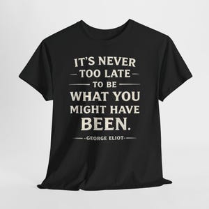 May include: Black t-shirt featuring the quote "IT'S NEVER TOO LATE TO BE WHAT YOU MIGHT HAVE BEEN." in white lettering, attributed to George Eliot. The shirt has a crew neck and short sleeves.