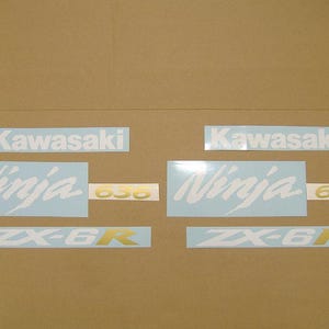 Puede incluir: Un conjunto de calcomanías para motocicletas Kawasaki Ninja. Las calcomanías incluyen el logotipo de Kawasaki, la palabra "Ninja", el número "636" y las letras "ZX-6R". El texto es blanco y dorado.