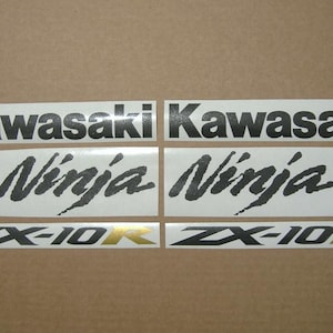 以下が含まれることがあります： カワサキNinja ZX-10Rオートバイ用デカールのセット。デカールには、黒色のカワサキロゴ、「Ninja」のスタイリッシュなフォント、金色のアクセントが付いた「ZX-10R」が含まれています。ニュートラルな背景です。