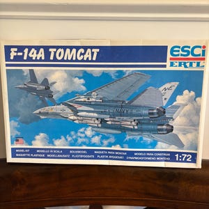 May include: A model kit box for an F-14A Tomcat aircraft. The box features a detailed illustration of the jet in flight, with the text "F-14A TOMCAT" prominently displayed. The box also includes the text "ESCI ERTL" and "1:72".