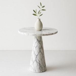 May include: A round marble side table with a white and gray veined pattern. The table has a conical base and a small, off-white vase with green leaves on top. The table is approximately 24 inches in diameter.