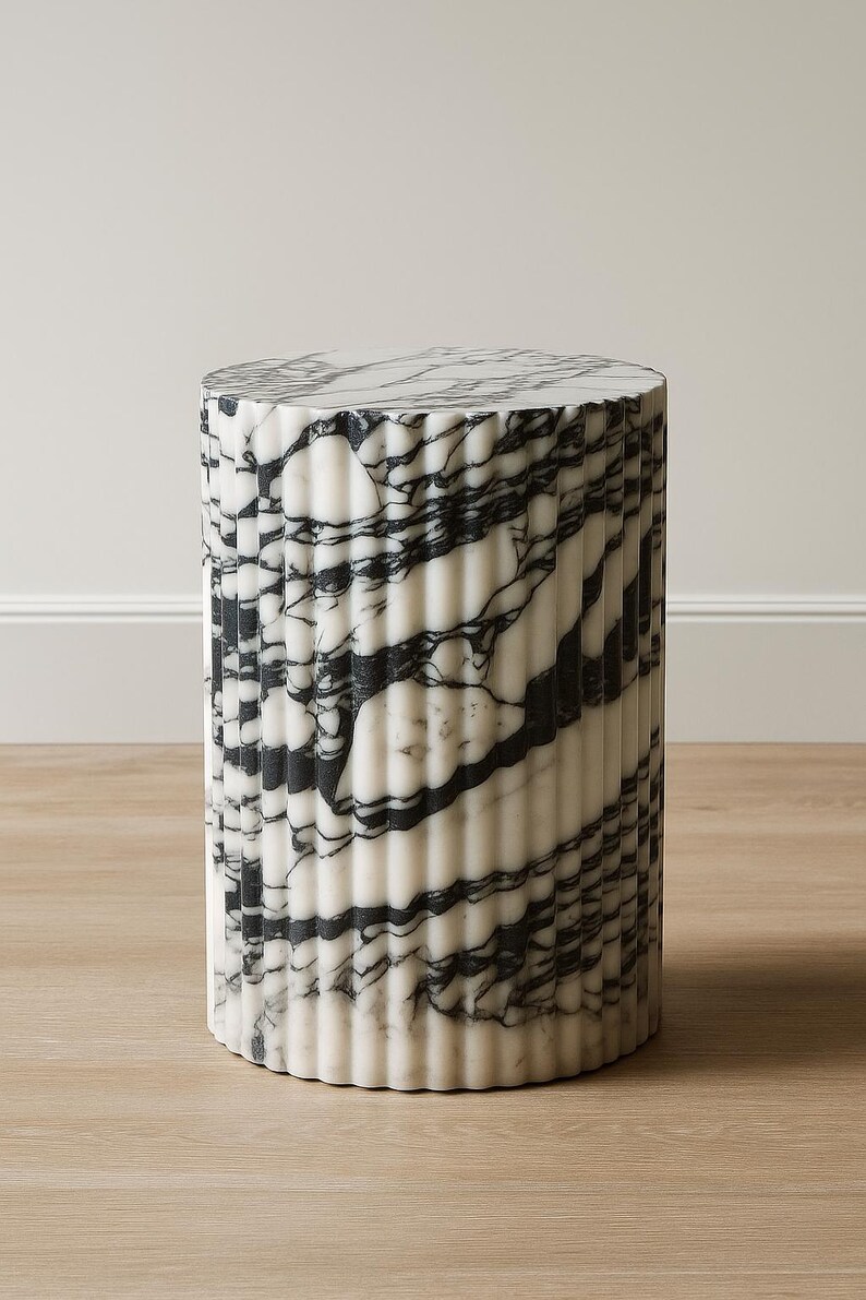 May include: A cylindrical marble side table with a fluted design. The table features a white base with black veining, and measures approximately 18 inches in height and 14 inches in diameter. The top surface is also marble.