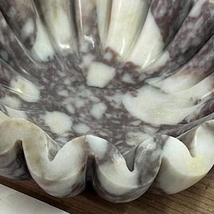 Pu&ograve; includere: Una ciotola decorativa a forma di conchiglia in marmo. La ciotola presenta un motivo naturale di tonalit&agrave; bianche, grigie e viola. I bordi ondulati e le venature uniche creano un forte impatto visivo. Questo pezzo artigianale &egrave; ideale per esporre piccoli oggetti.