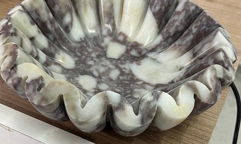 Pu&ograve; includere: Una ciotola decorativa a forma di conchiglia in marmo. La ciotola presenta un motivo naturale di tonalit&agrave; bianche, grigie e viola. I bordi ondulati e le venature uniche creano un forte impatto visivo. Questo pezzo artigianale &egrave; ideale per esporre piccoli oggetti.