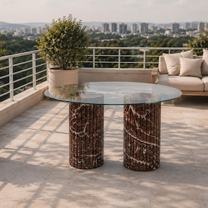 Könnte beinhalten: Moderner Outdoor-Tisch mit klarer Glasplatte und zwei zylindrischen Sockeln aus braunem und weißem Marmor. Der Tisch steht auf einer Terrasse mit Blick auf die Stadt im Hintergrund. Für den Außenbereich konzipiert.