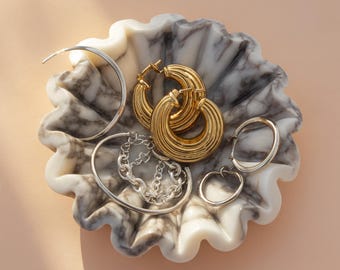 May include: A collection of gold and silver earrings and bracelets displayed in a decorative marble bowl. The earrings include large gold hoop earrings, small silver hoop earrings, and a silver chain bracelet. The bowl has a white and gray marbled pattern.