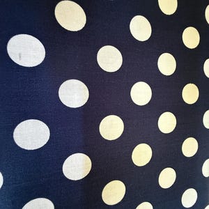May include: A navy blue fabric with a white polka dot pattern. The dots are evenly spaced and are a consistent size.