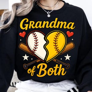Puede incluir: Sudadera negra con un gráfico de un corazón roto hecho de pelotas de béisbol. El texto "Grandma of Both" está impreso debajo del corazón.