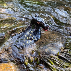 Puede incluir: Una figurita de cerámica negra de un caballo con detalles pintados en oro, parcialmente sumergida en una corriente de agua poco profunda.